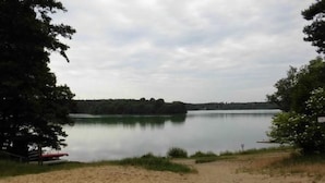 Una spiaggia sabbiosa con un lago calmo, circondata da alberi e una costa in lontananza.