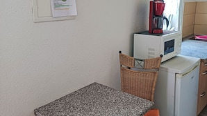 Un angolo cottura con forno a microonde, un piccolo frigorifero e una sedia in vimini.