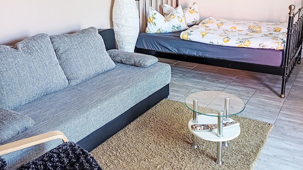 Una camera da letto moderna con un divano, un letto con lenzuola fantasia, un tavolino in vetro e un'ampia finestra.