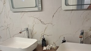 Ett badrum med två handfat, väggar klädda i marmor och skåp i trä.
