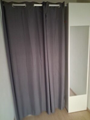 Quarto com cortina cinza, guarda-roupa branco e chão de madeira.