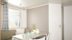 A small, modern room with a white table, a white chair, a window with a curtain, and a door. - Mobilheim Lagune II in Lychen by Interhome (Lychen)