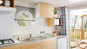 A compact kitchen with wooden cabinets, a built-in sink, and a window. - Mobilheim Lagune I in Lychen by Interhome (Lychen)