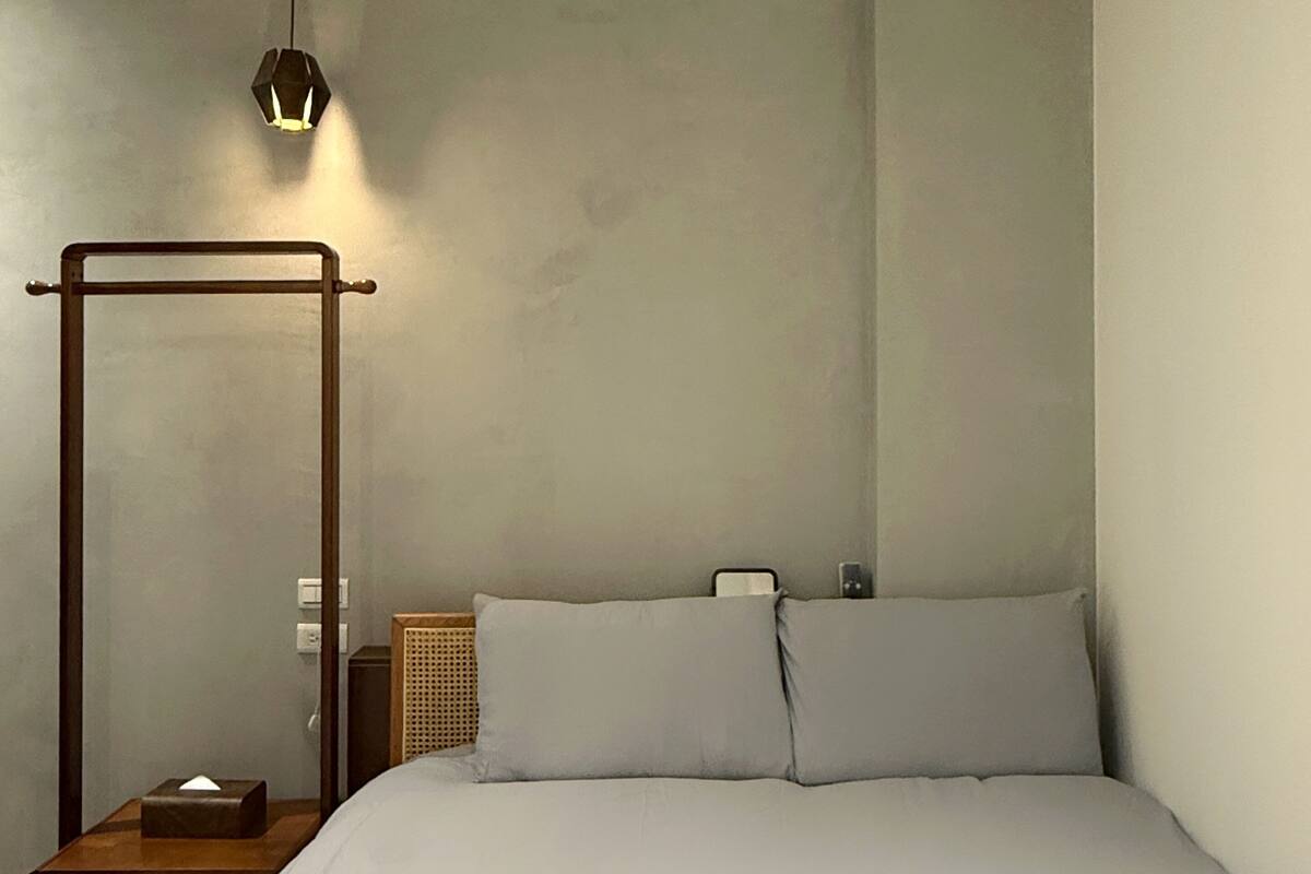 Un dormitorio con cama con dosel, una mesita de noche con lámpara y otra mesita más pequeña con un pañuelero.