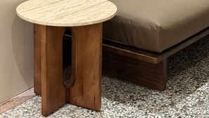 Esquina de una habitación con un sofá marrón y una pequeña mesa de madera con tapa redonda.