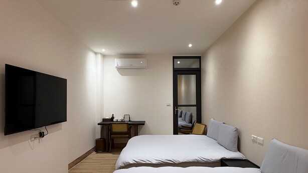 Habitación de hotel moderna con dos camas, un televisor de pantalla plana montado en la pared, un escritorio con una silla y un equipo de aire acondicionado.