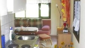 A compact kitchen with a stove, sink, and a small dining area with a chair and table. - Ferienhäuschen am Strandbad Lychen, Bungalow by Interhome (Lychen)