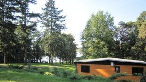 A small wooden cabin with a sloped roof, surrounded by dense trees and grassy area. - Ferienhäuschen am Strandbad Lychen, Bungalow by Interhome (Lychen)