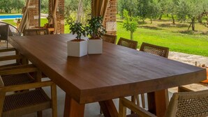 Un espacio para comer al aire libre con una mesa y sillas de madera, un muro de ladrillo y vistas a un paisaje verde.