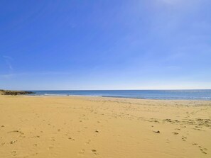 Ein weiter Sandstrand mit Fußspuren und einem strahlend blauen Himmel.