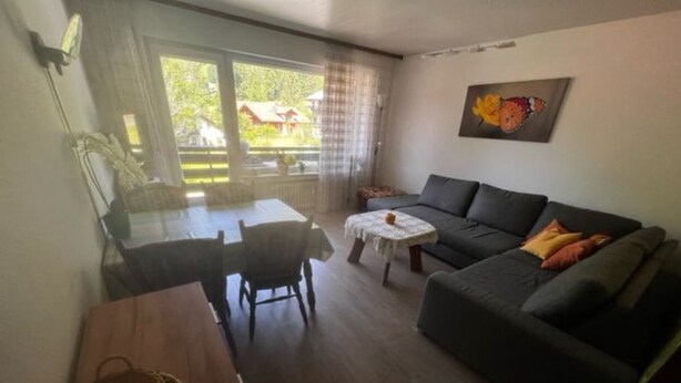A living room with a dark grey sofa, a small table, and a dining table with chairs. - Sonnenbichl Wh 102 by Interhome (Oberstdorf)