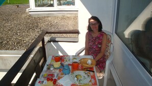 Una mujer sentada a una mesa con comida, una ventana y vistas a un paisaje verde.