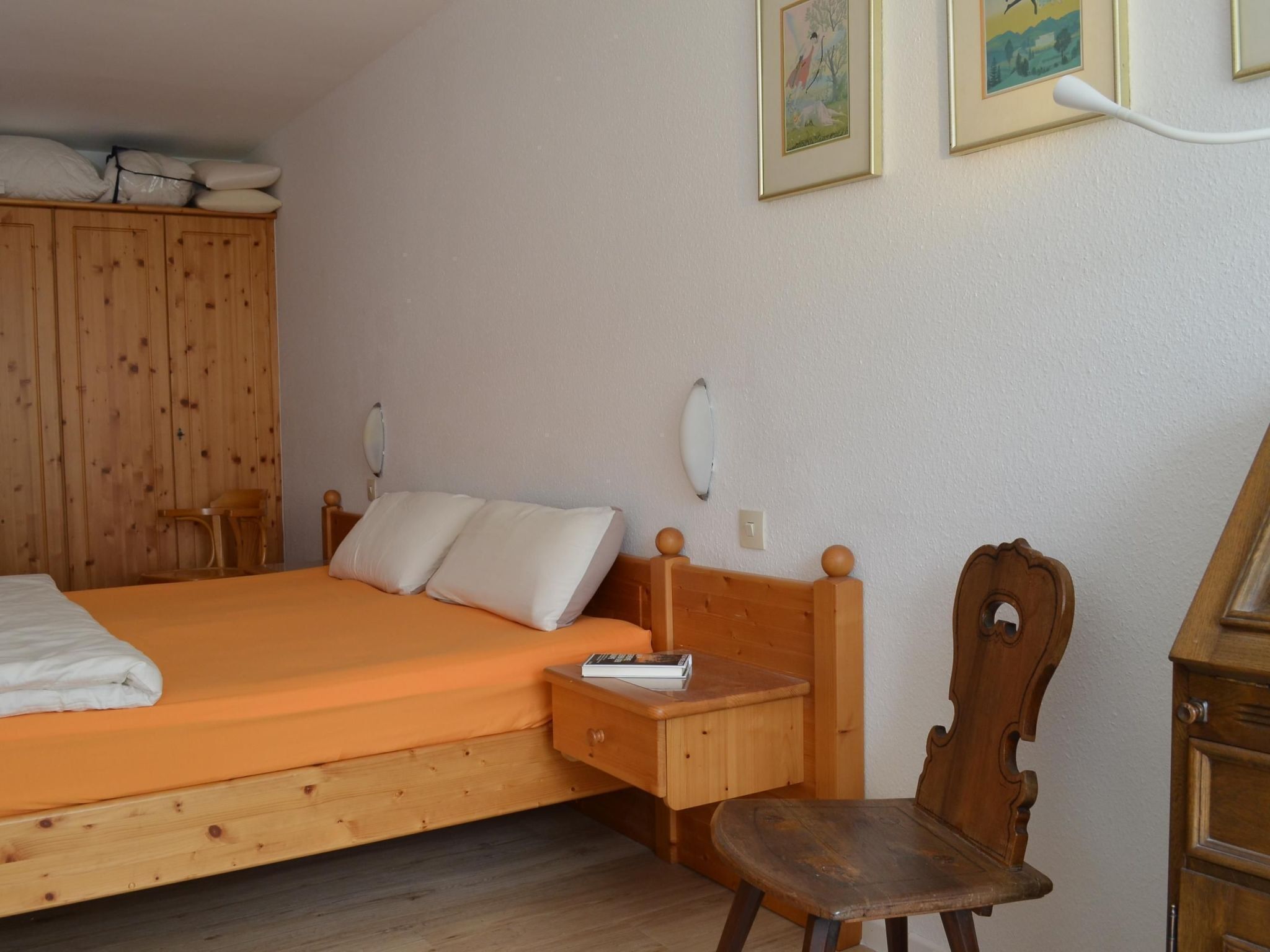 Ein Schlafzimmer mit einem hölzernen Bett, einem Nachttisch aus Holz, einem Stuhl, einem Holzschrank und zwei gerahmten Bildern an der Wand.