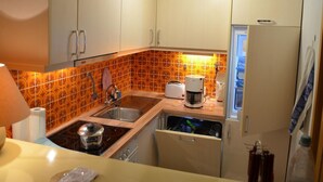 Cocina compacta con armarios blancos, estufa, fregadero y refrigerador.