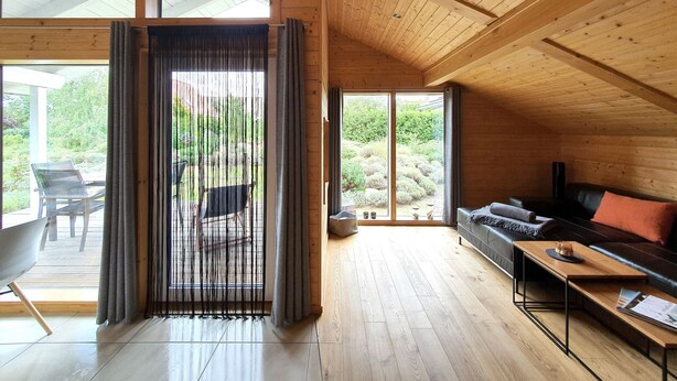 A spacious room with wooden floors and a sloped ceiling, featuring a sofa, a dining table, and a large window with curtains. - "Gartenglück" by Interhome (Alt Jassewitz)