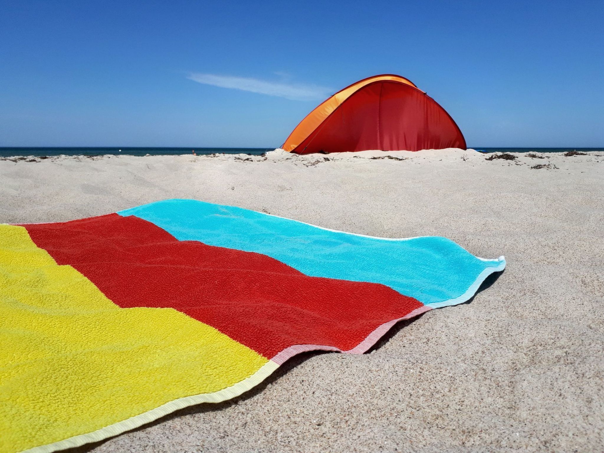 Une plage avec une serviette colorée et une tente rouge.