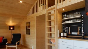 A cozy cabin interior with a wooden ceiling, a dining table, a kitchen area with shelves, and a chair. - "Gartenglück" by Interhome (Alt Jassewitz)