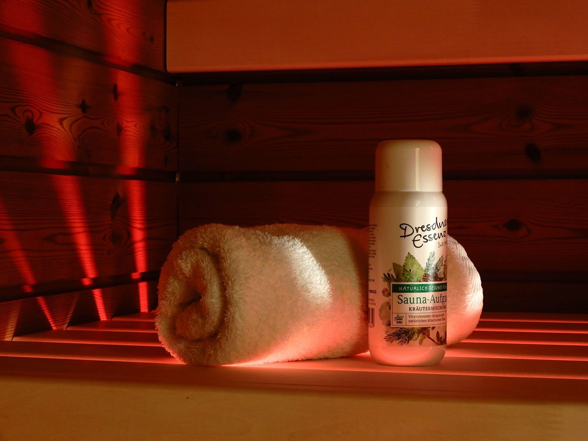 Un estante de madera con una toalla enrollada y una botella de Dresdner Essenz Sauna-Aqua.