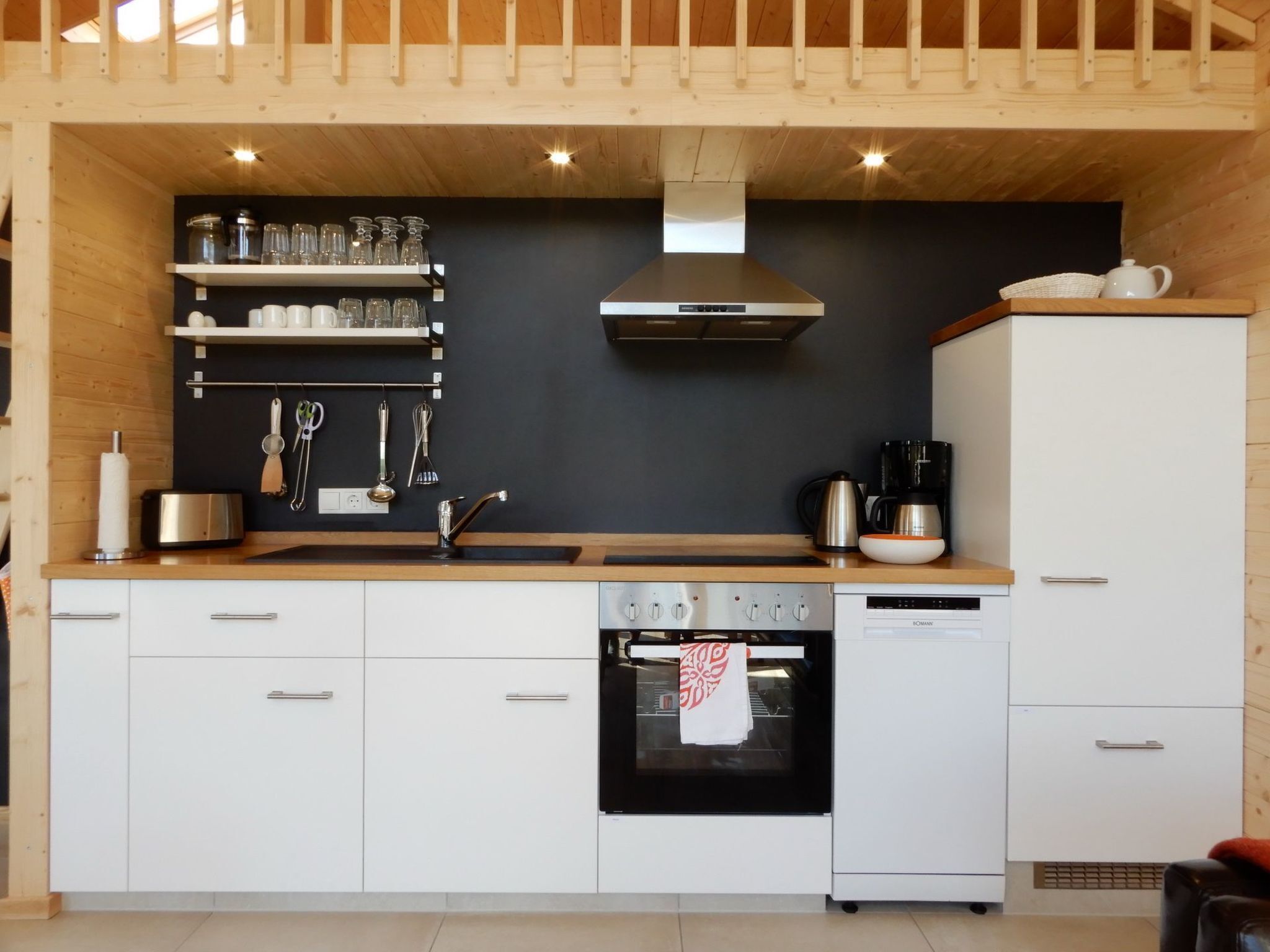 A modern kitchen with white cabinets, a stainless steel range, a black oven, and a coffee maker.