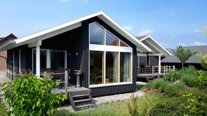 Ett modernt hus med ett stort glasfönster, en terrass och en trädgård.