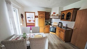 Una cocina compacta con armarios de madera, una mesa de comedor con sillas de mimbre y vista al dormitorio contiguo.