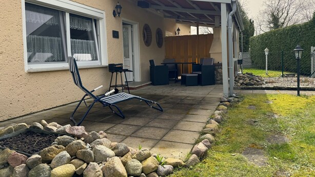 A covered patio area with outdoor furniture, a stone pathway, and a garden bed with rocks. - Hans am Klostersee by Interhome (Dargun)