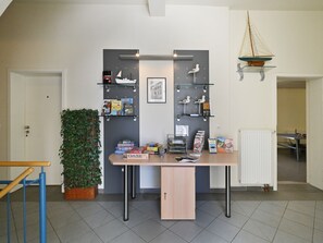 Ein Zimmer mit Schreibtisch, Regalen mit Büchern und Spielen, einer Pflanze und einem Schiffsmodell.
