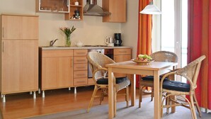 Una cocina compacta con armarios de madera, una mesa de comedor con sillas de mimbre y vistas al exterior a través de una ventana.