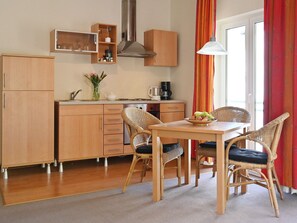 Eine kompakte Küche mit Holzausstattung, einem Esstisch mit Korbstühlen und Blick ins Freie durch ein Fenster.