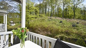 Een wit terras buiten met een tafel en stoelen, met uitzicht op een bebost landschap.