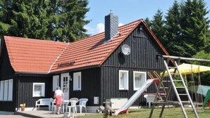 Musta puinen rakennus, jossa on punainen katto, valkoiset ikkunat ja liukumäki pihalla.