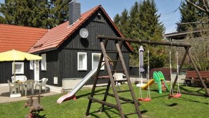 Leikkikentällä on keinut ja liukumäki, piknikpöytä sekä punaisella katolla varustettu rakennus.