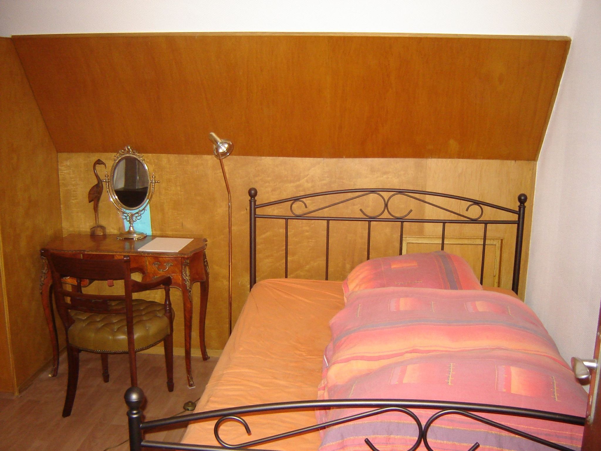 A bedroom with a bed, a wooden desk with a mirror, and a chair.