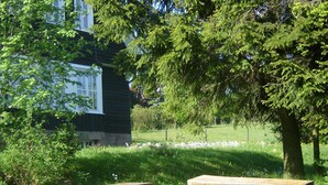 Een houten bank in het gras, met een huis op de achtergrond.
