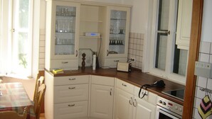 Een keuken met witte kasten, een houten aanrechtblad, een raam en een betegelde achterwand.