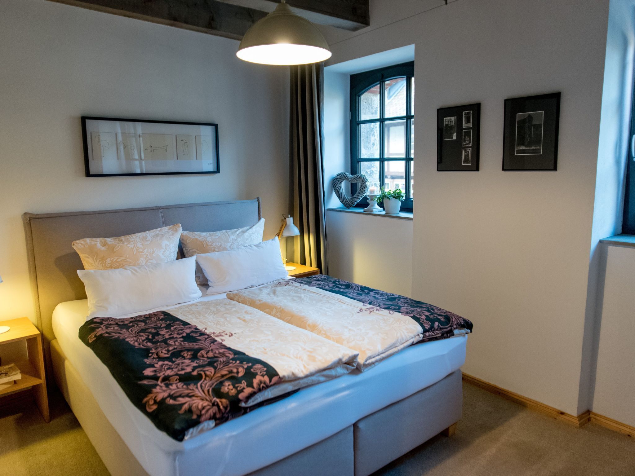 A neatly made bed with a floral bedspread, a bedside table with a lamp, and a window with curtains.