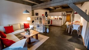Ein großzügiger Wohnbereich mit Sofa, Couchtisch und Bücherregal. Im Hintergrund sind eine Küche und ein Essbereich zu sehen.