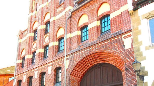 Ein historisches Gebäude mit einem markanten Bogenportal, einer Stein-Fassade und zahlreichen Fenstern.