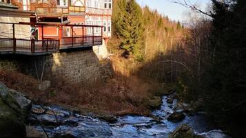 Ein traditionelles Gebäude mit roter Fassade und mehreren Balkonen, gelegen neben einem Fluss mit felsigem Ufer.
