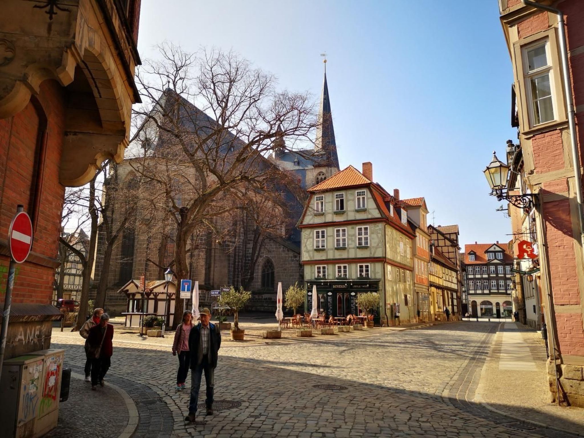 A cobblestone street with historic buildings, a church spire, and a no-entry sign.