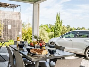 En uteservering med ett bord dukat för två personer, ett bröd, frukt och olika tillbehör.