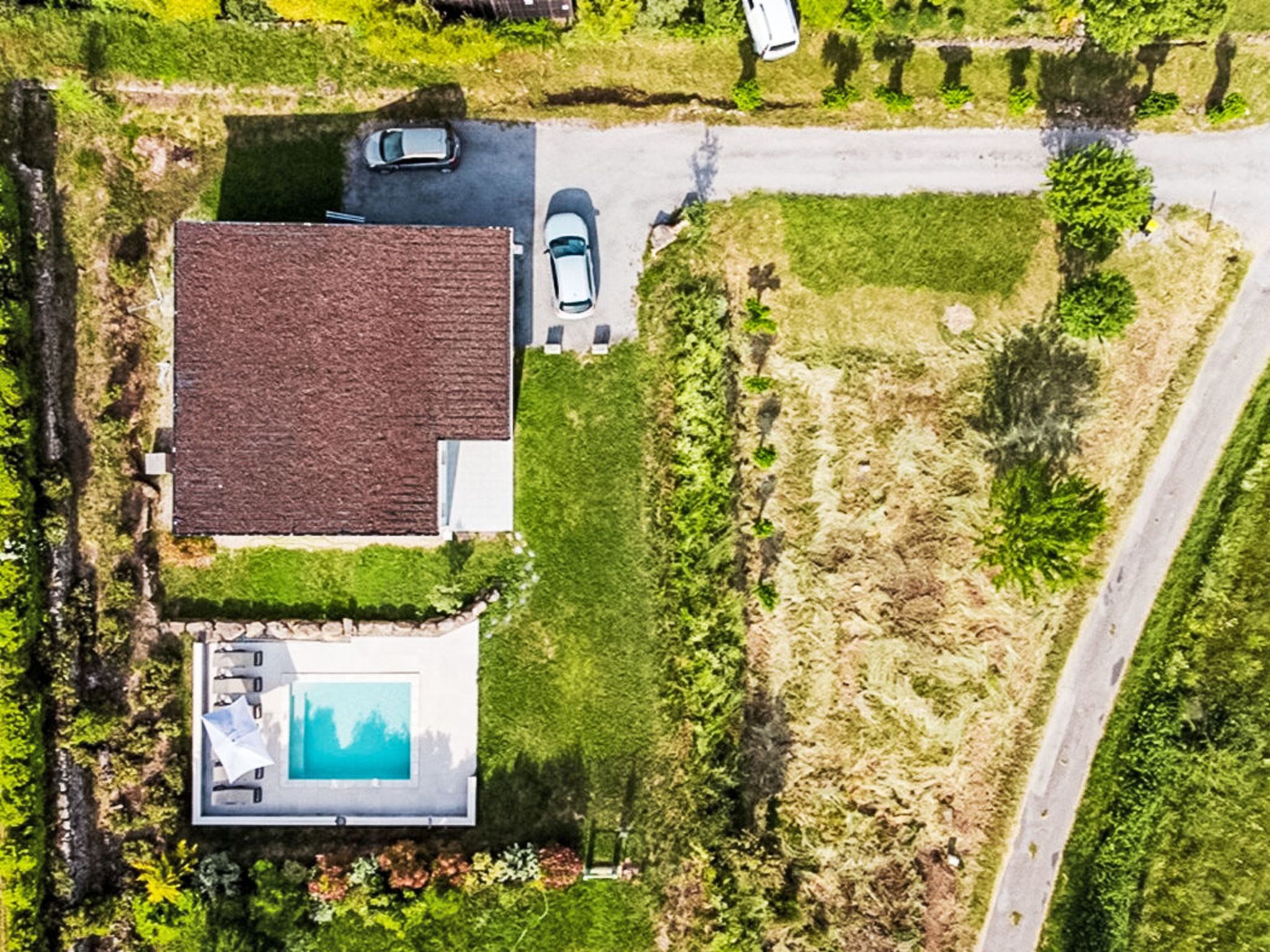 Eine Luftaufnahme eines Hauses mit Swimmingpool, Auffahrt und einer Straße.
