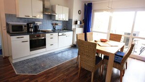 Een moderne keuken met witte kasten, roestvrijstalen apparatuur en een eethoek met rieten stoelen en een houten tafel.