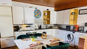 Cozinha compacta com armários brancos, máquina de lavar e espaço de jantar com mesa e cadeiras.