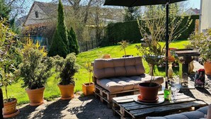 Uma área de varanda externa com um sofá estofado, uma mesa de madeira e plantas em vasos.