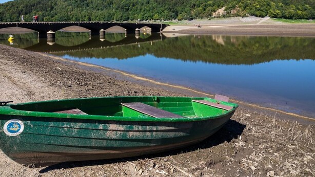 Um barco verde numa praia arenosa, com uma ponte ao fundo.