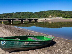 Un bote verde sobre una orilla arenosa con un puente al fondo.
