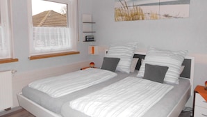 A bedroom with two single beds, a window with a view of a building, a bedside table with a lamp, and a wall-mounted shelf. - Apartment  by Interhome (Diemelsee)