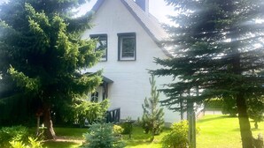 Una casa bianca con tetto a due falde, circondata da alberi sempreverdi e un prato curato.