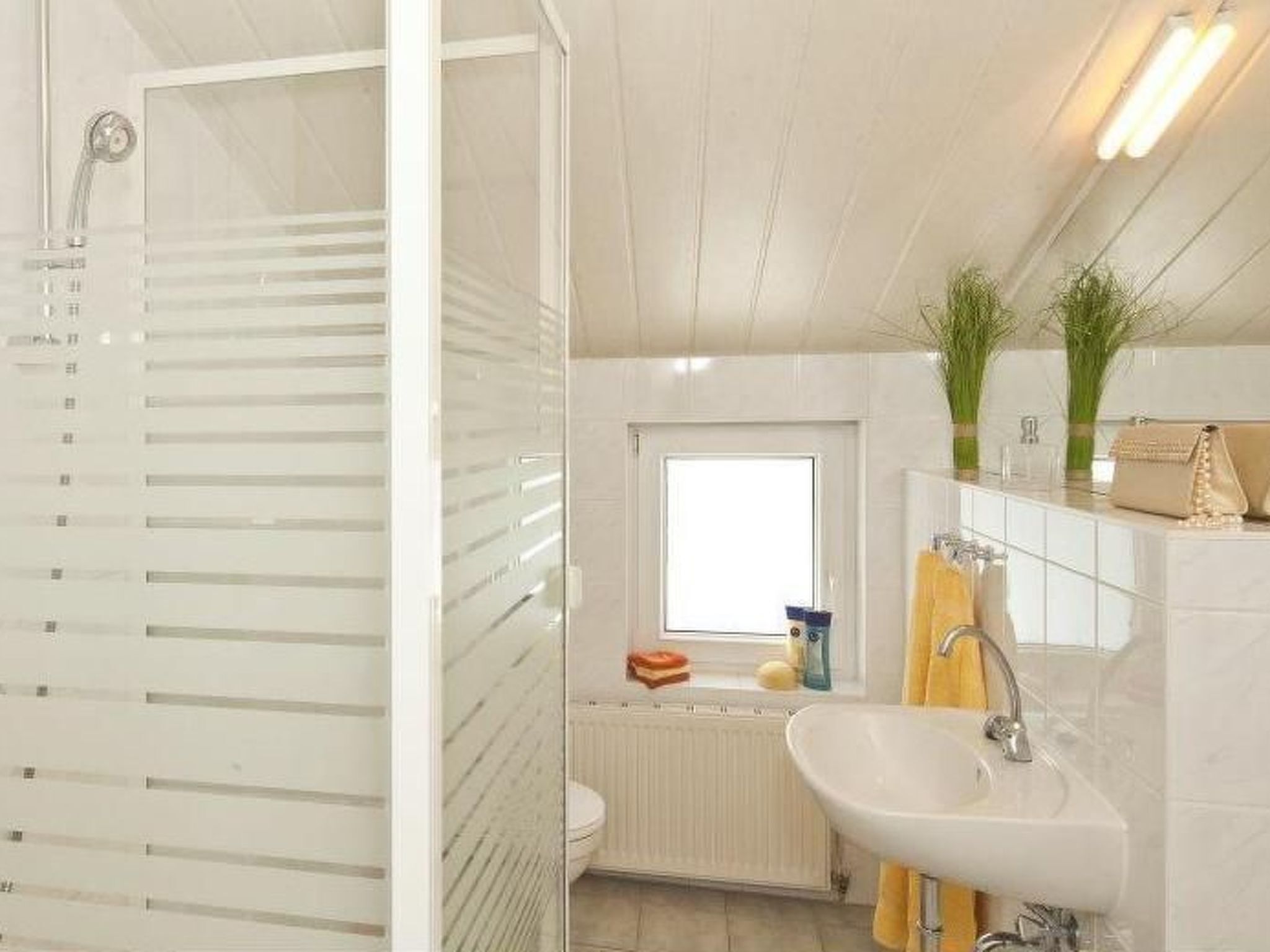A bathroom with a glass shower enclosure, a white sink, and a window providing natural light.